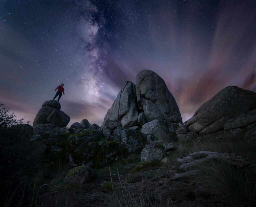 Young man standing on a rock at nighttime with the milky way above